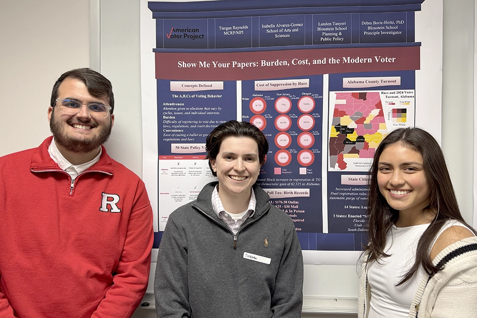 Landon Tanyeri, B.S. Public Policy candidate; Tiergan Reynolds, MCRP/MPI candidate; Isabella Alvarerz-Gomez, B.S. Public Policy candidate, first place winners of graduate best poster competition, stands in front of their colorful poster titled "Show Me Your Papers: Burden, Cost, and the Modern Voter."